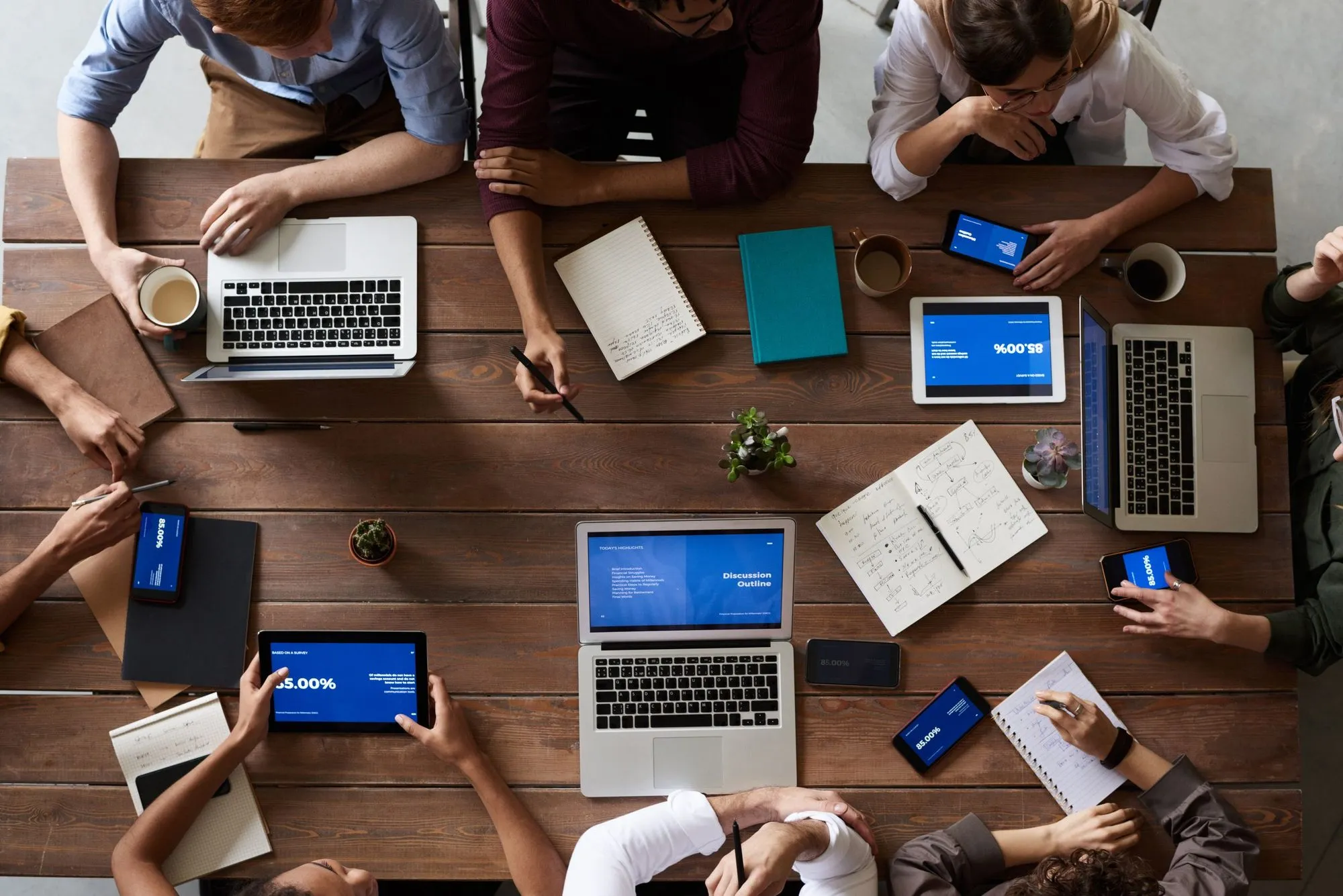 Top view of people around a wooden table with laptops and notebooks